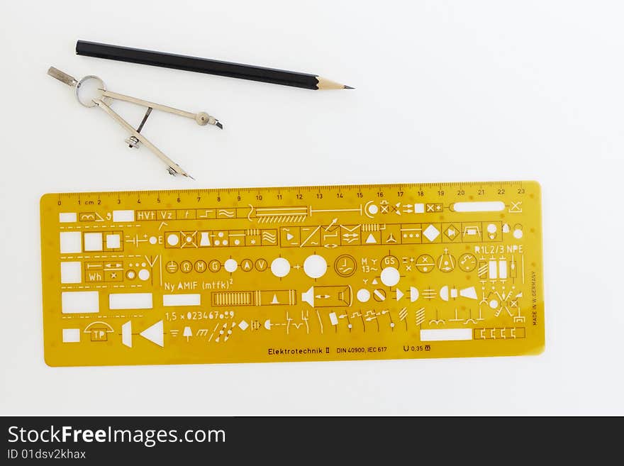 Drafting instruments and an electronic symbol stencil on a piece of paper. Two pairs of compasses a stencil and a pencil are laid out in a symmetrical pattern. Drafting instruments and an electronic symbol stencil on a piece of paper. Two pairs of compasses a stencil and a pencil are laid out in a symmetrical pattern.