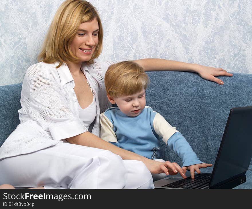 Young mum with the small beautiful boy together sit near laptop. Young mum with the small beautiful boy together sit near laptop