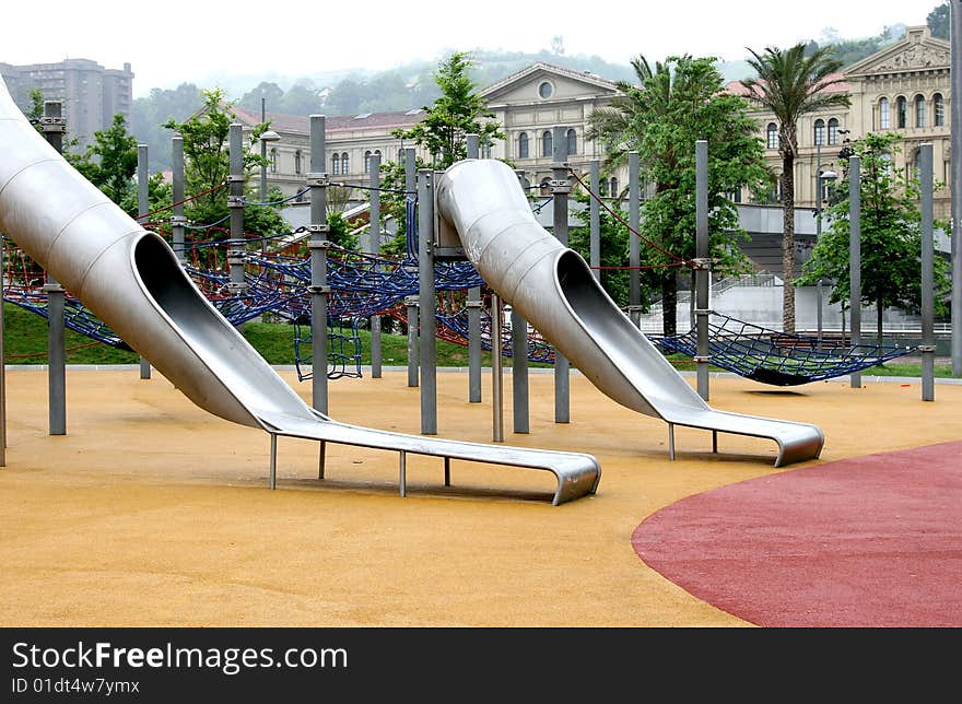 A child friendly play area with chutes and rope ladders in the centre of Bilbao in spanish Basque Country. Green trees and palms are surrounding the children's playground. A child friendly play area with chutes and rope ladders in the centre of Bilbao in spanish Basque Country. Green trees and palms are surrounding the children's playground.