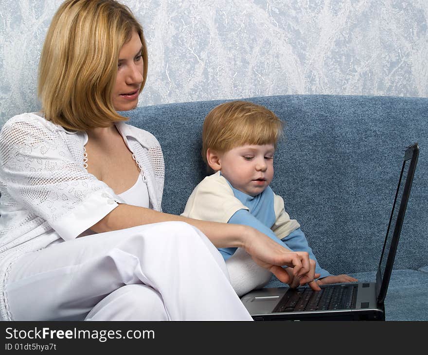 Young mum with the small beautiful boy together sit near laptop. Young mum with the small beautiful boy together sit near laptop