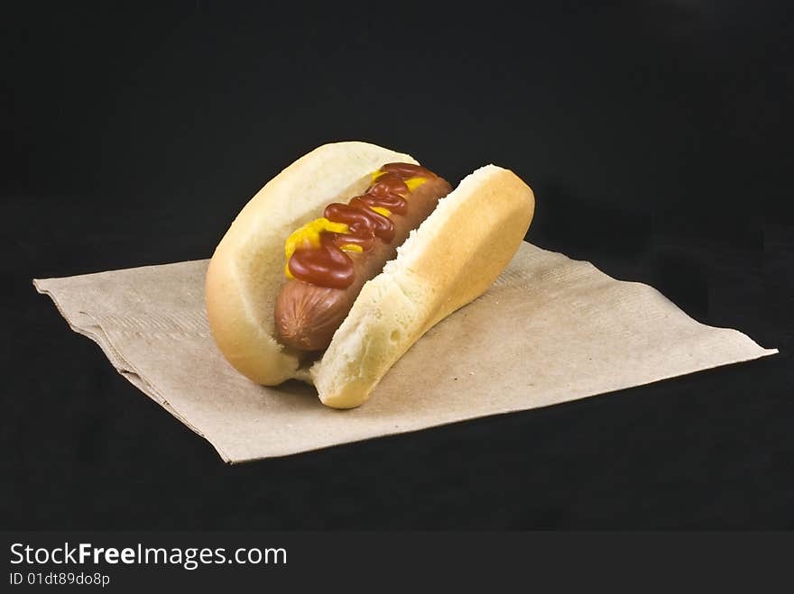 Hotdog with ketchup and mustard in a hotdog bun on a black background.