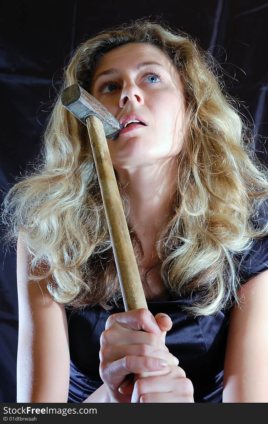 Young sexy woman bites a hammer against a black background. Young sexy woman bites a hammer against a black background