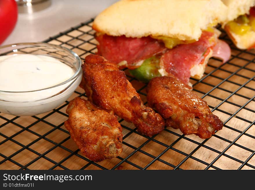 Hot spicy buffalo style chicken wings in front of bowl of Blue Cheese dressing and deli sandwich. Hot spicy buffalo style chicken wings in front of bowl of Blue Cheese dressing and deli sandwich.