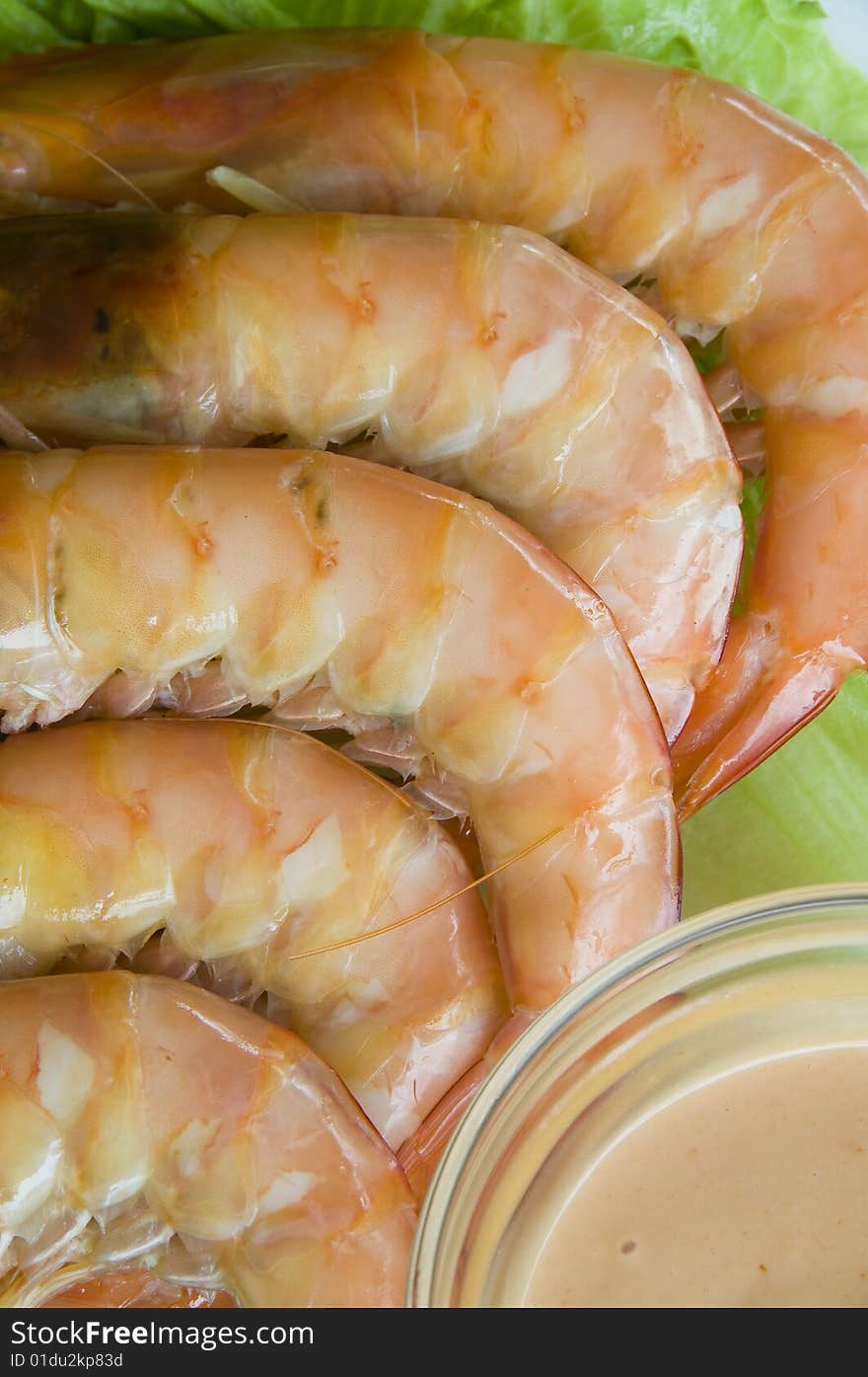 Fresh king prawns placed on a bed of lettuce served with a pink sauce and slices of lemons accompanied by a glass of white wine in an outdoor setting.