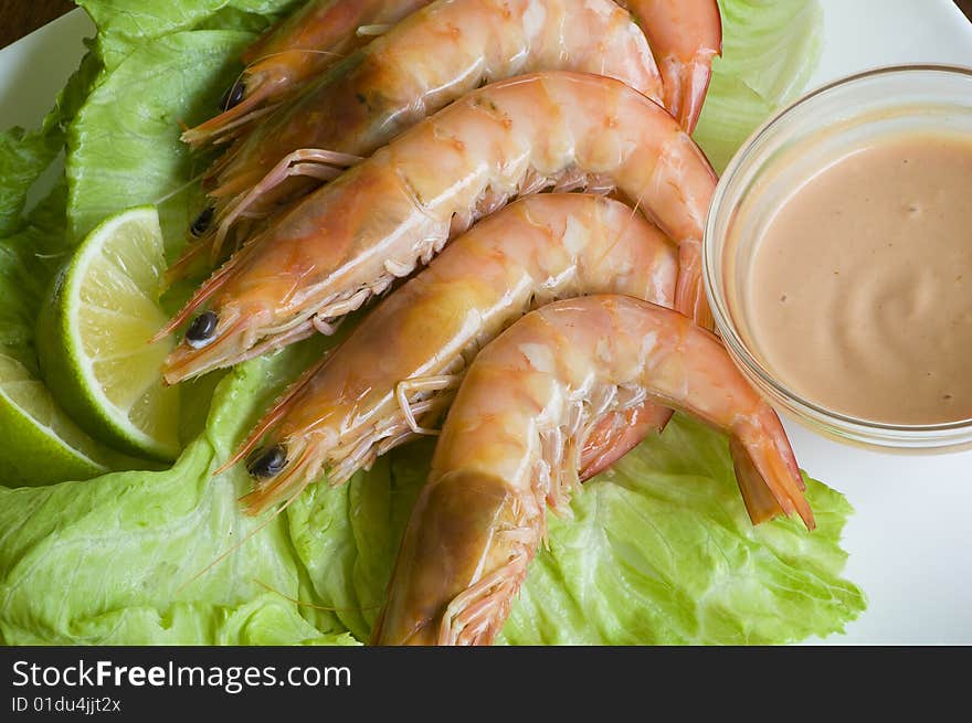 Fresh king prawns placed on a bed of lettuce served with a pink sauce and slices of lemons accompanied by a glass of white wine in an outdoor setting.