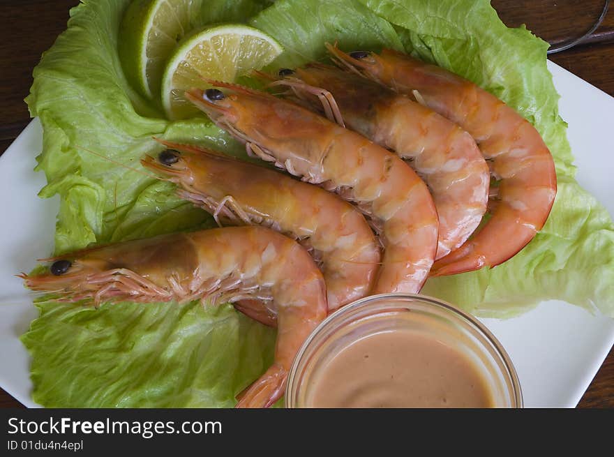 Fresh king prawns placed on a bed of lettuce served with a pink sauce and slices of lemons accompanied by a glass of white wine in an outdoor setting.