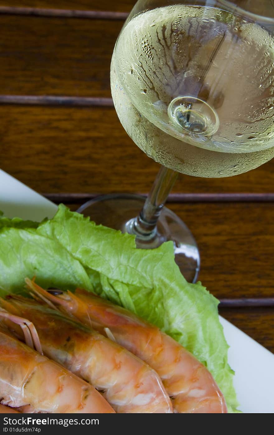 Fresh king prawns placed on a bed of lettuce served with a pink sauce and slices of lemons accompanied by a glass of white wine in an outdoor setting.