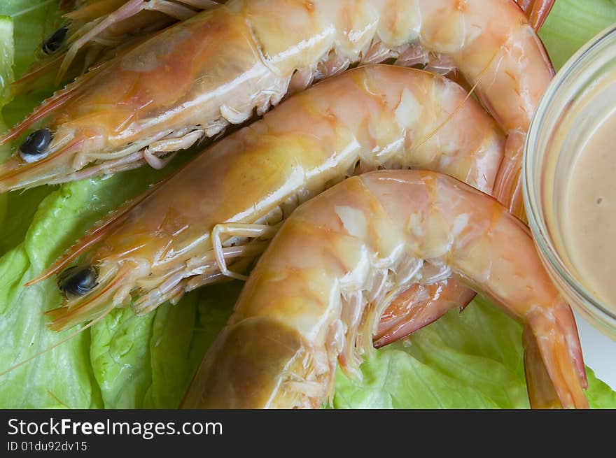 Fresh king prawns placed on a bed of lettuce served with a pink sauce and slices of lemons accompanied by a glass of white wine in an outdoor setting.