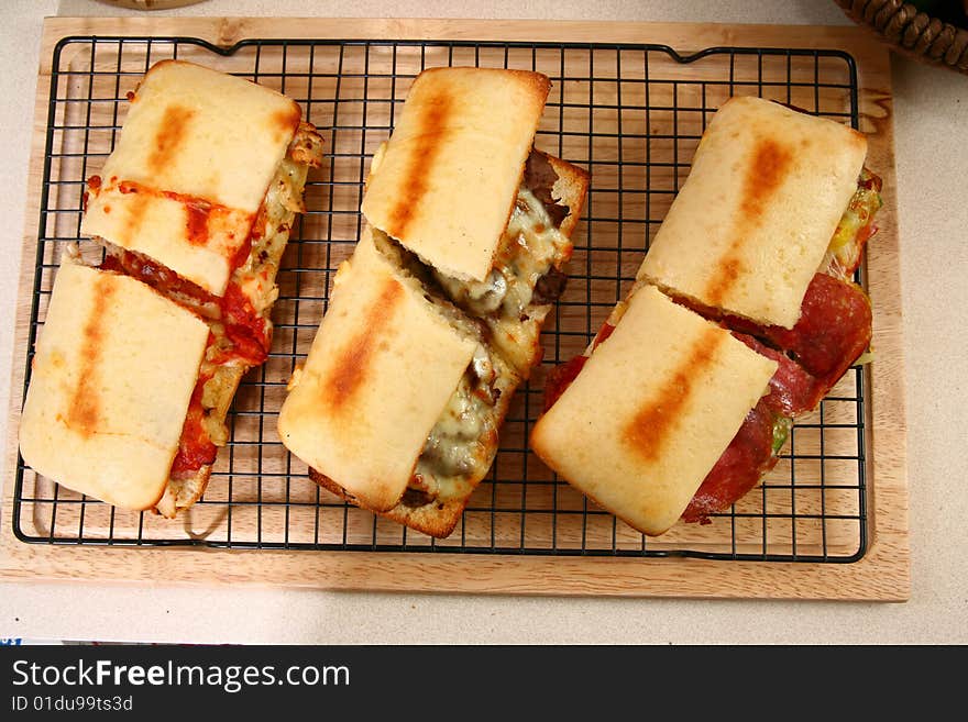 Various toasted submarine sandwiches with chicken, beef, ham, sausage, melted cheese, vegetables, and marinara sauce.