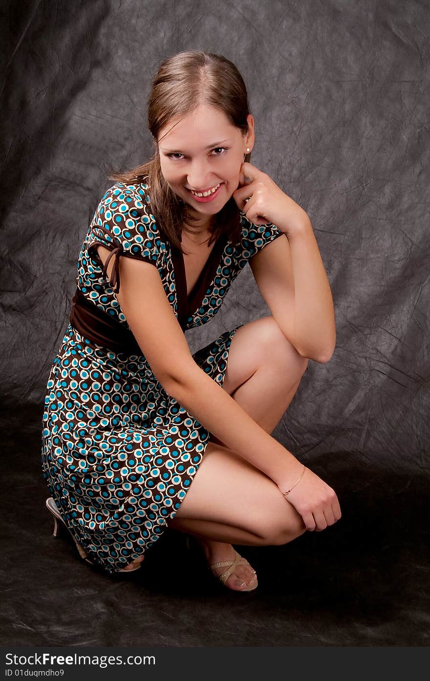 Young white girl in color dress sitting on her hunkers turned slightly smiling isolated on black