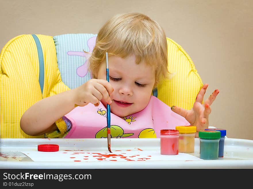 The child of 2 years sits in a children's chair and draws paints. The child of 2 years sits in a children's chair and draws paints