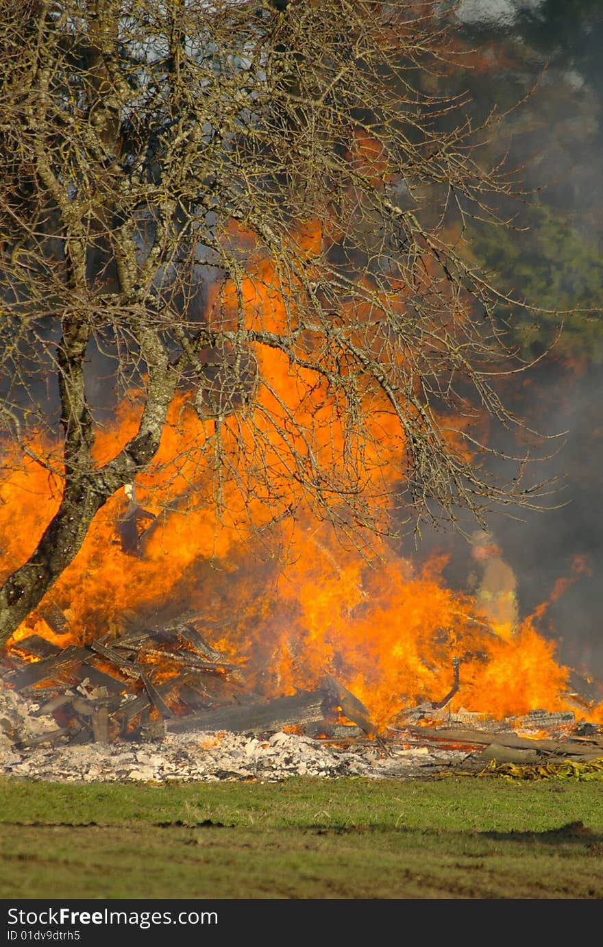 A fireman blurred out by the heat of the flames walks past whats left of a house engulfed in flames. A fireman blurred out by the heat of the flames walks past whats left of a house engulfed in flames.