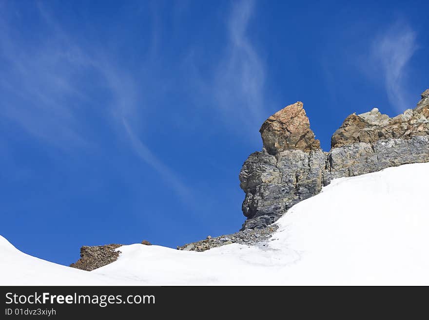 Snow landscape with rocks in Swiss Alps, bright blue sky in background with copy-space