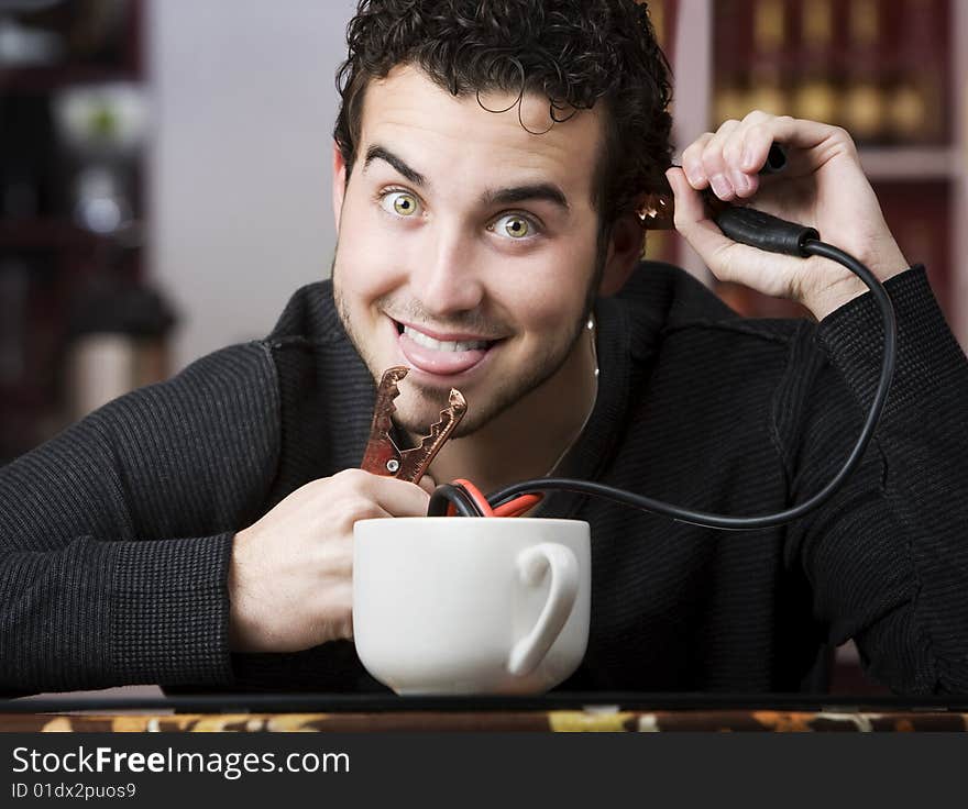 Young man holding jumper cables coming out of coffee mug. Young man holding jumper cables coming out of coffee mug