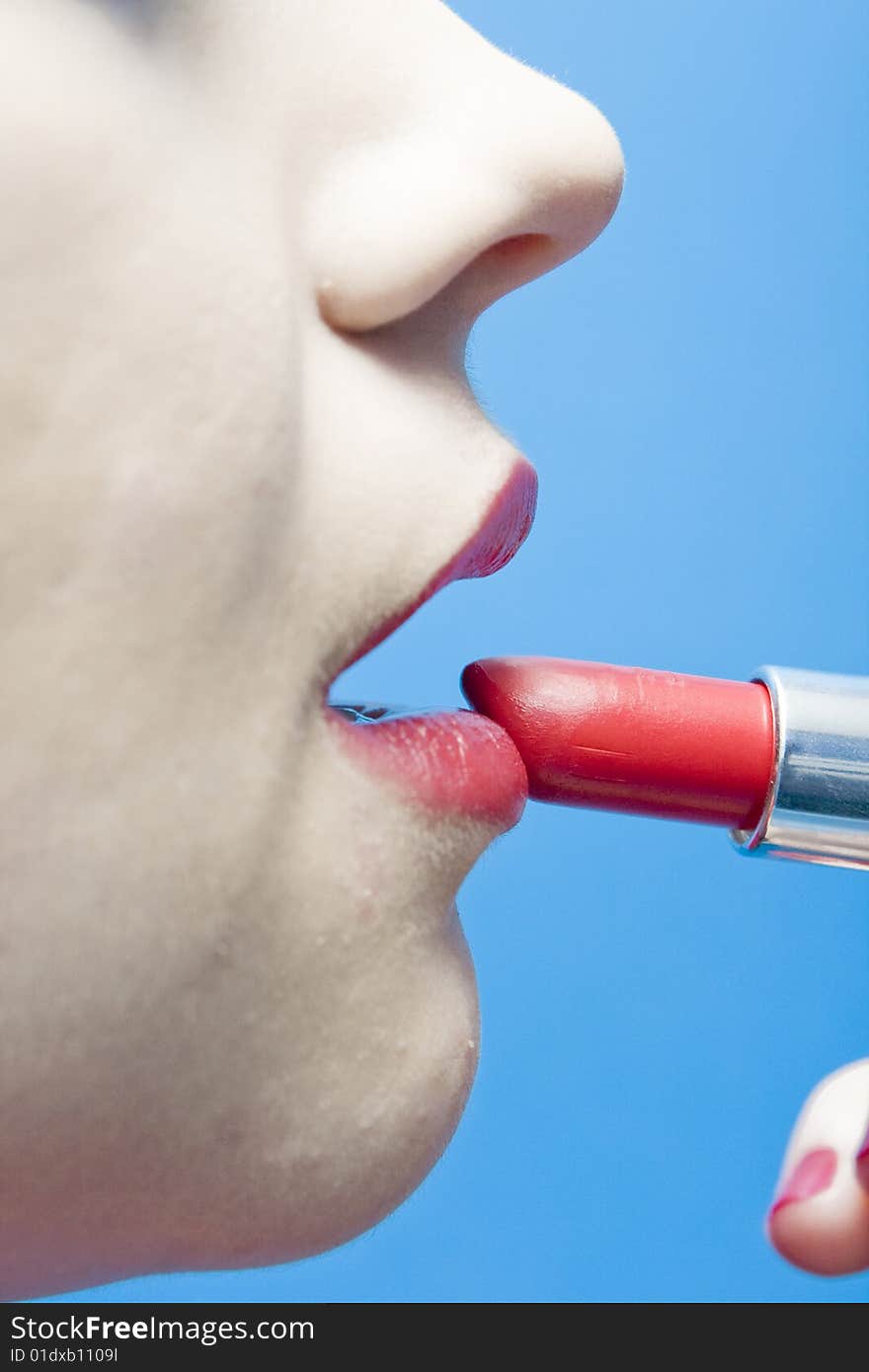 Closeup of a woman applying lipstick on a blue background