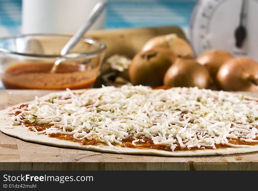 Uncooked pizza laying on wooden board with ingredients