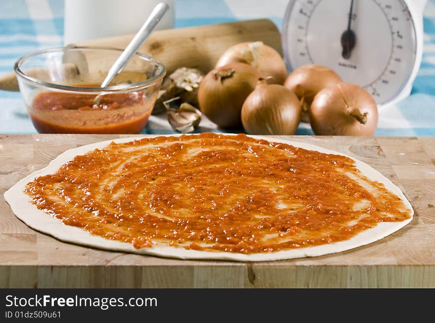 Uncooked pizza laying on wooden board with ingredients