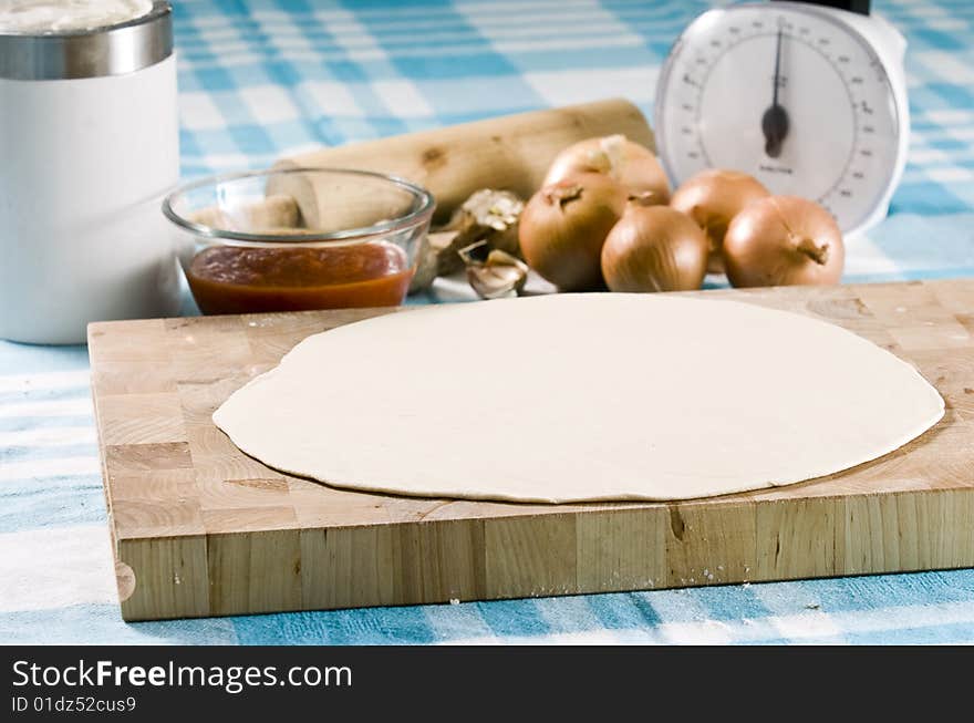 Uncooked pizza laying on wooden board with ingredients