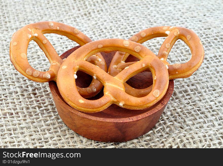 Three pretzels in the wooden bowl, on the sack cloth