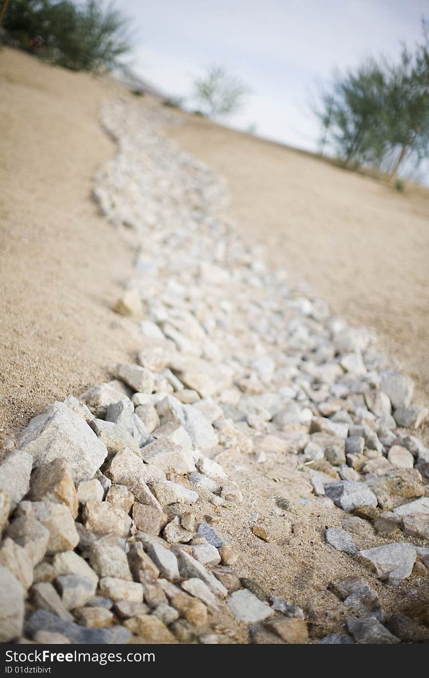 A rock path made of many different tan rocks and sand line a simple path down a hill