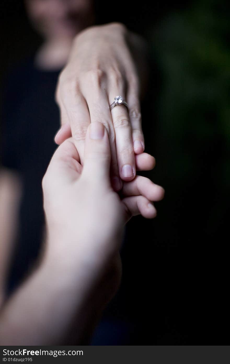 A woman holds her hand up to show her wedding ring as a man holds her hand up to see the ring. A woman holds her hand up to show her wedding ring as a man holds her hand up to see the ring
