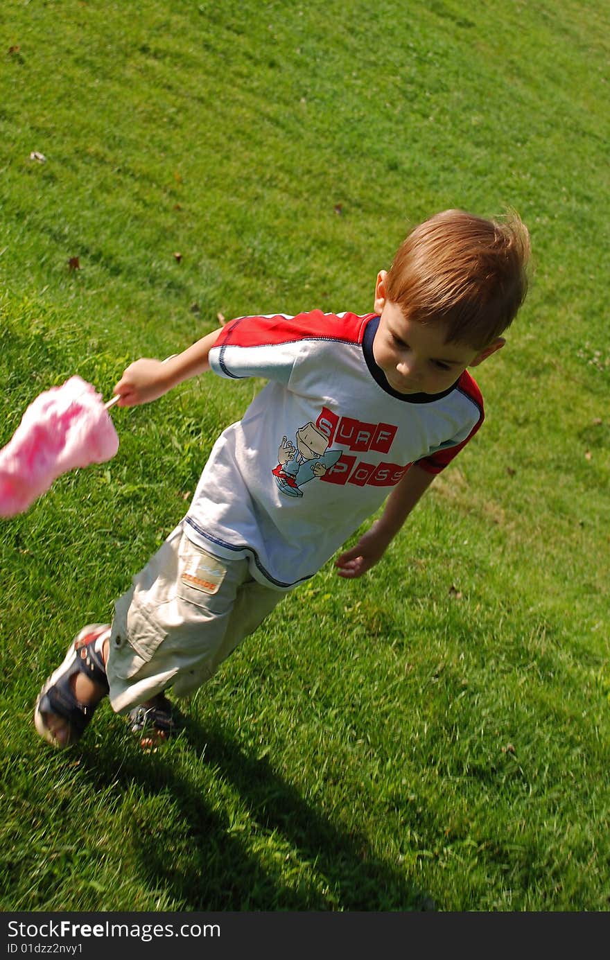 Child with cotton candy running on green grass field