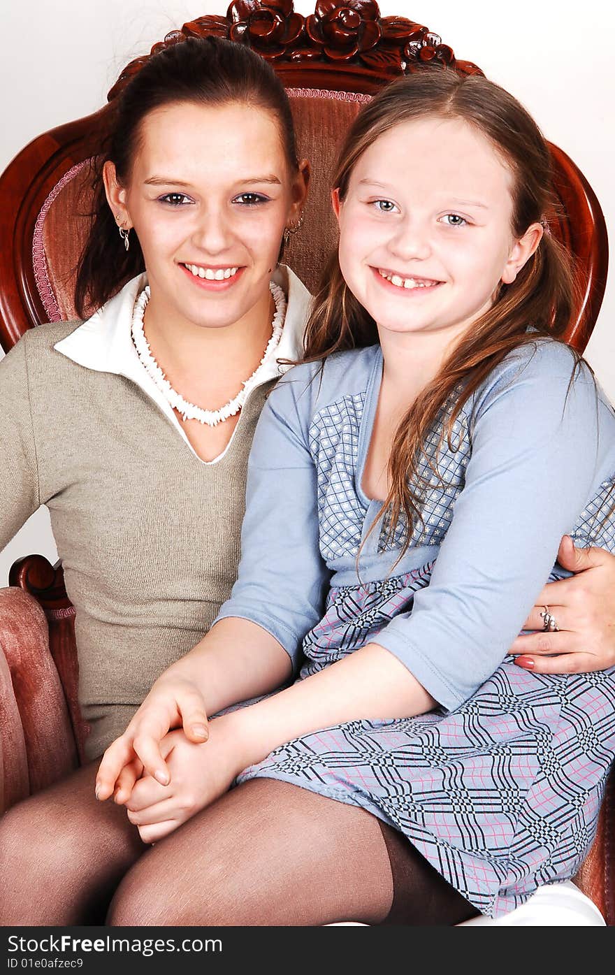 A happy smiling daughter sitting on the lap of her mother in an pink armchair. A happy smiling daughter sitting on the lap of her mother in an pink armchair.