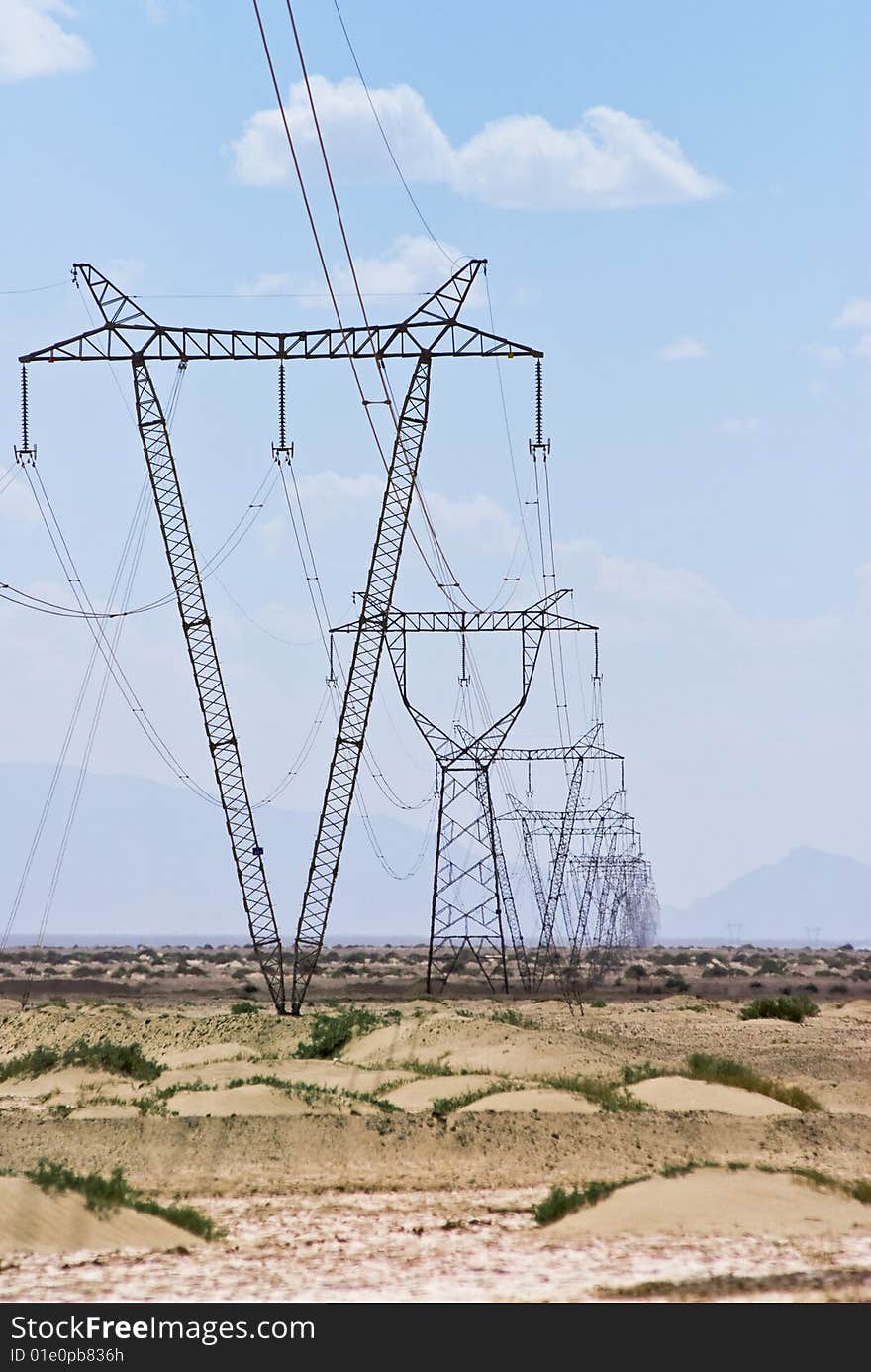 Power lines and array of electric pylons against a blue sky in desert. Power lines and array of electric pylons against a blue sky in desert