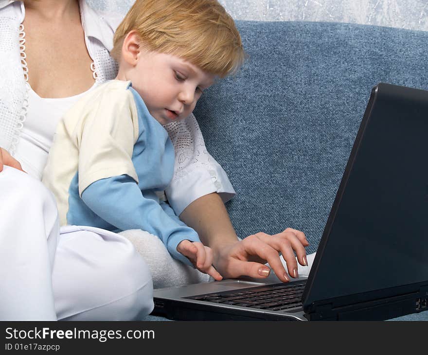 Young mum with the small beautiful boy together sit near laptop. Young mum with the small beautiful boy together sit near laptop