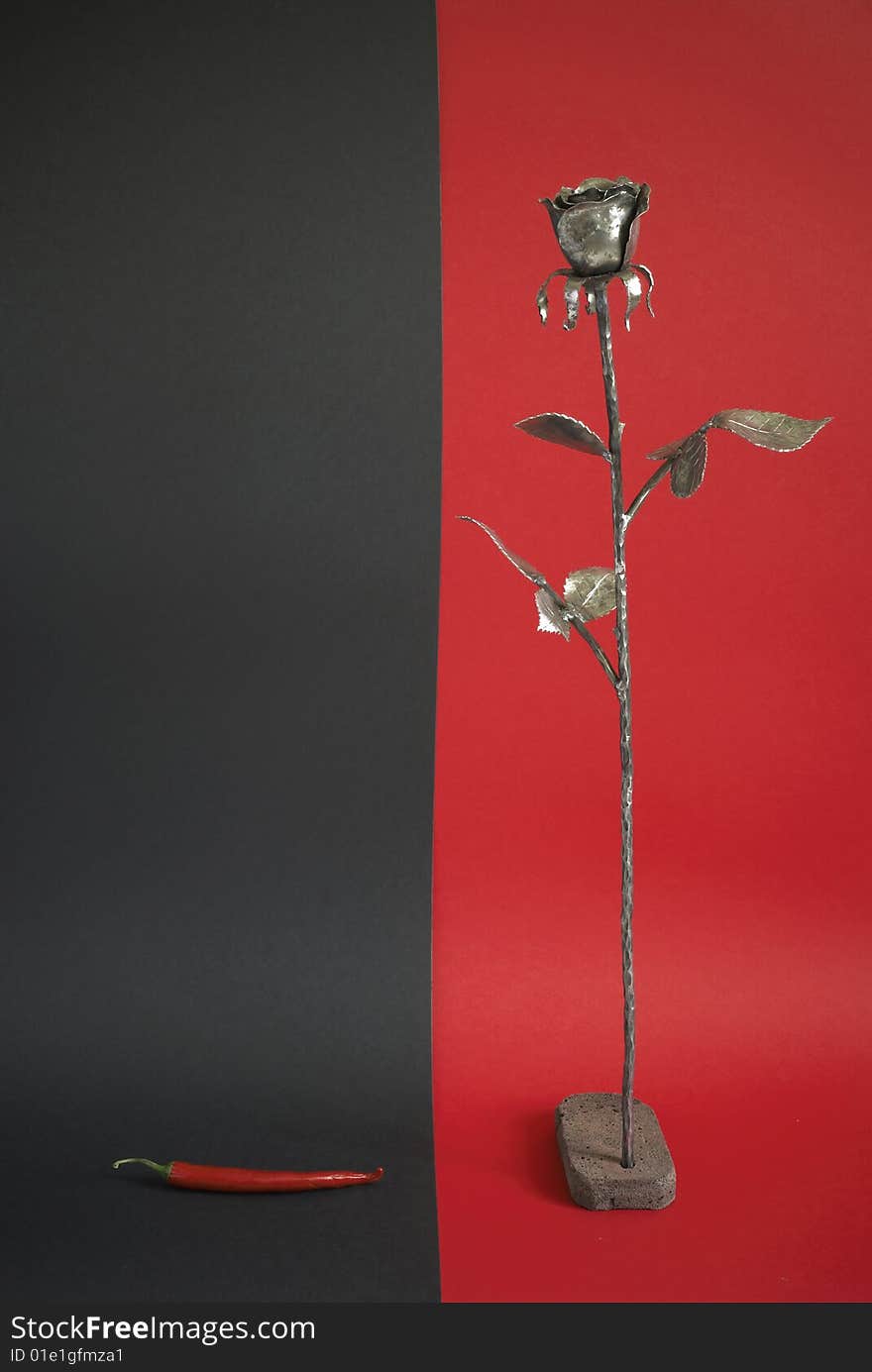 Iron rose and chili pepper on red and black background