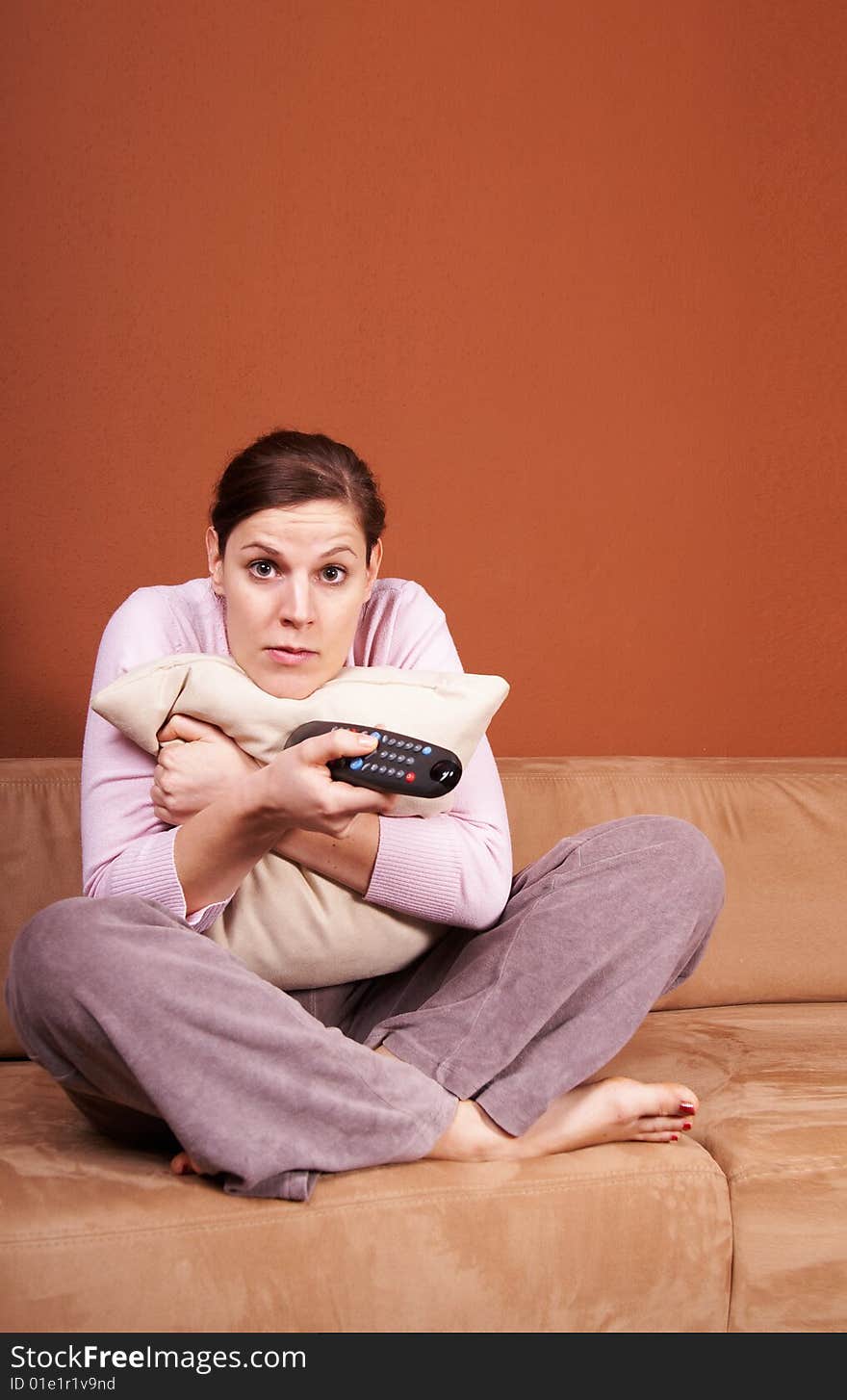 A young woman sits in front of a TV with the remote control in her hand on a couch. A lot of copyspace left. She seems to be afraid. A young woman sits in front of a TV with the remote control in her hand on a couch. A lot of copyspace left. She seems to be afraid.