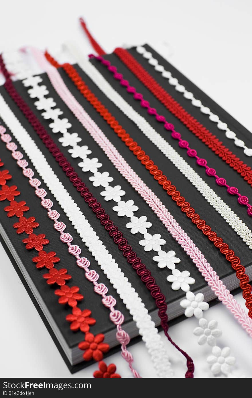 A detail of several red, pink and white embroidery - laces on dark fabric background - sewing supplies. A detail of several red, pink and white embroidery - laces on dark fabric background - sewing supplies.