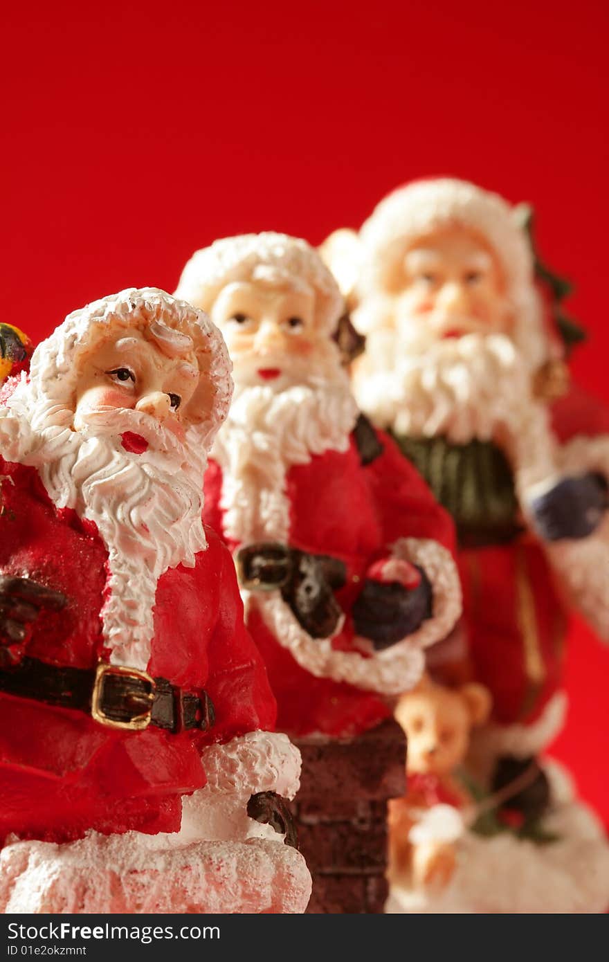 Three Santa Claus figurines over red background, studio shot