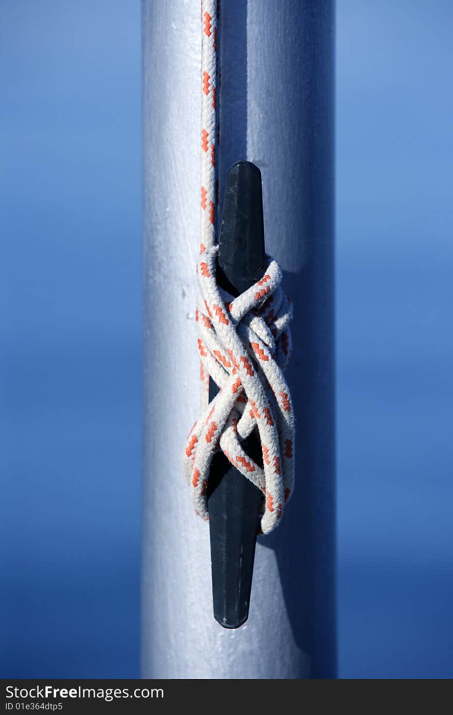 Marine rope, knot arround a steel pole, blue water background