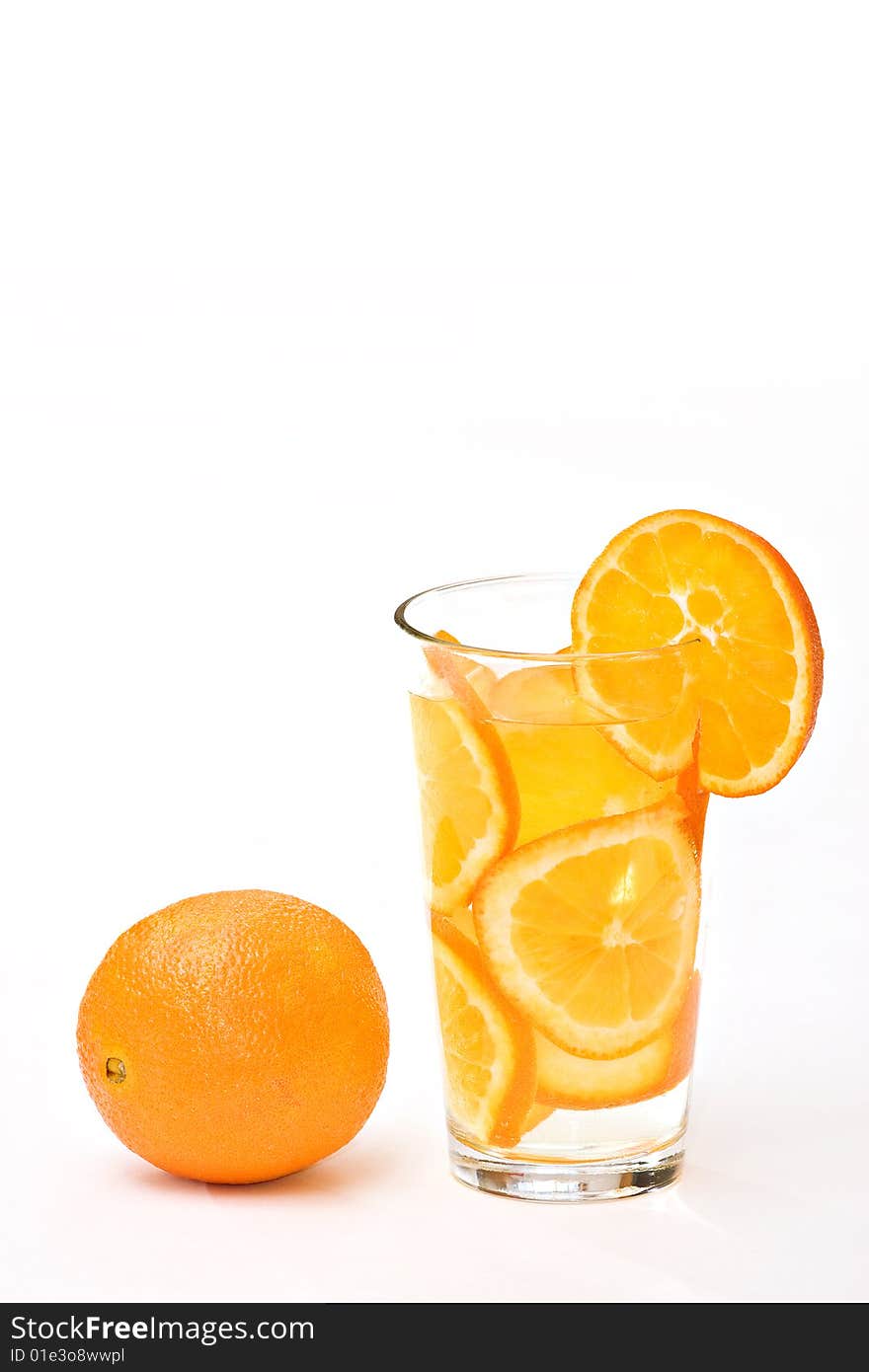 A drinking glass of orange slices and whole orange on white.