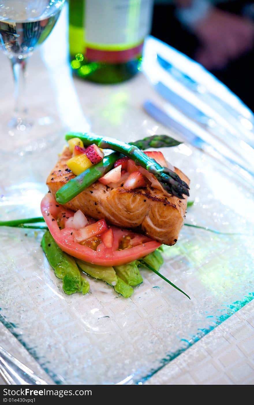 An image of fresh salmon on a bed of avocado and tomato topped with asparagus and fruit. An image of fresh salmon on a bed of avocado and tomato topped with asparagus and fruit