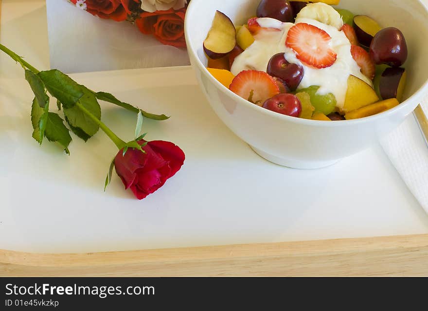 A tray of fruit and juice placed on a heart themed bed with rose and card for a romantic breakfast in bed