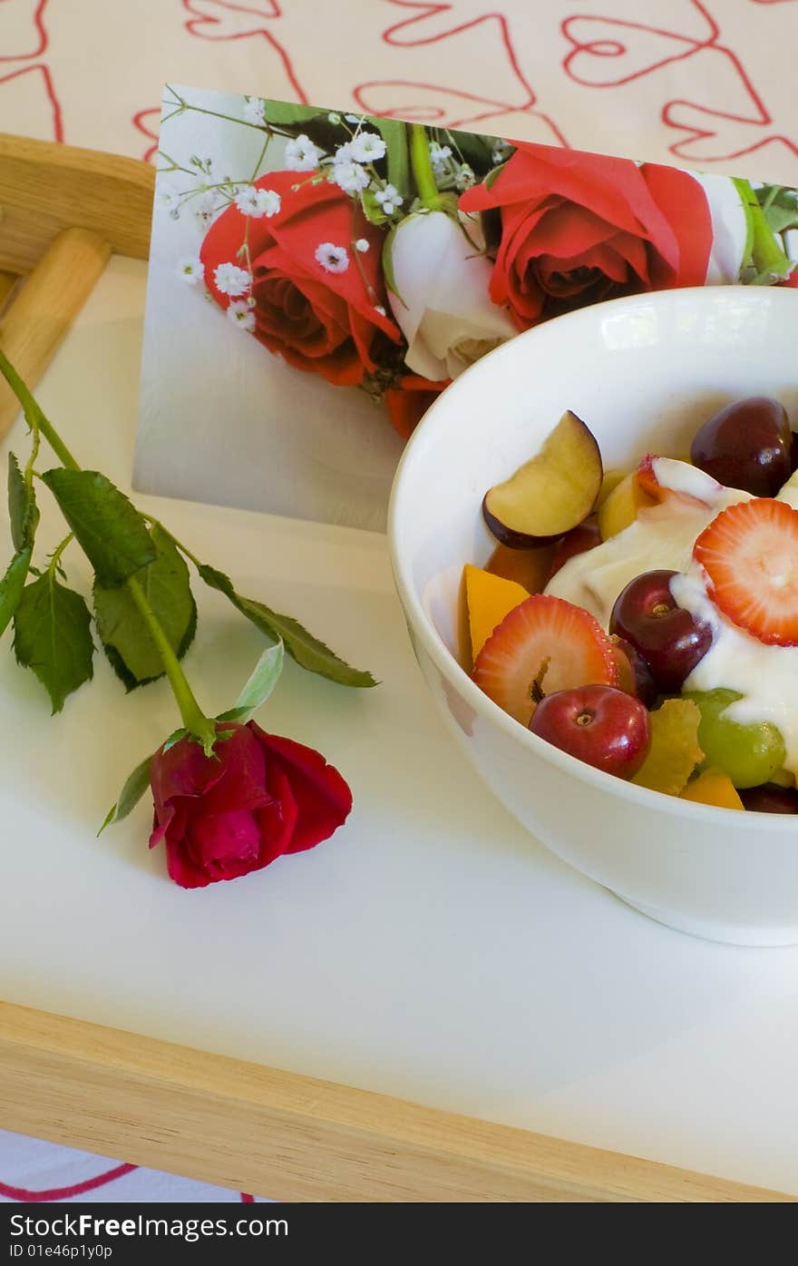 A tray of fruit and juice placed on a heart themed bed with rose and card for a romantic breakfast in bed