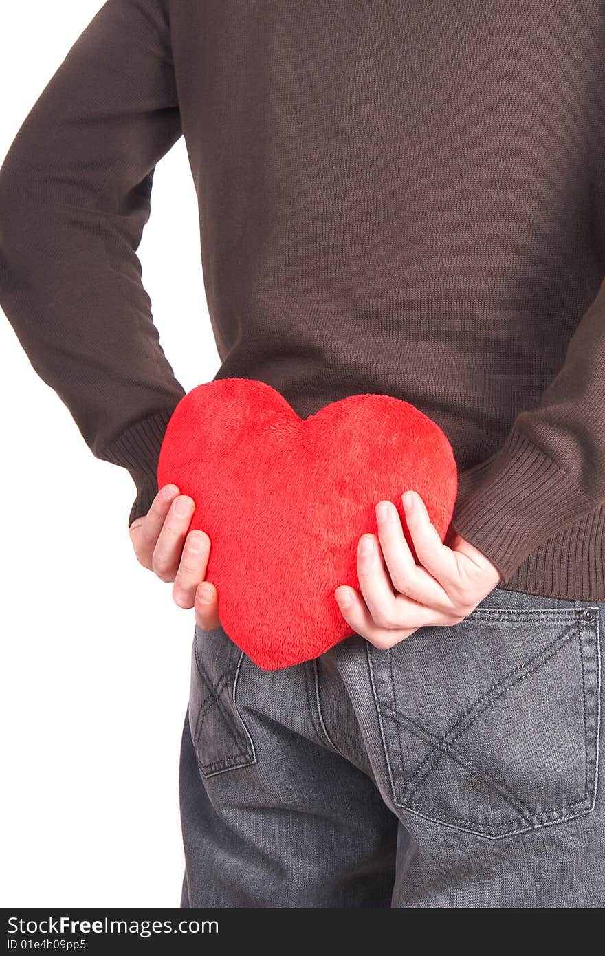 A young man holds a heart shaped pillow behind his back which he gives as a present to his girlfriend for valentines day. Isolated over white. A young man holds a heart shaped pillow behind his back which he gives as a present to his girlfriend for valentines day. Isolated over white.