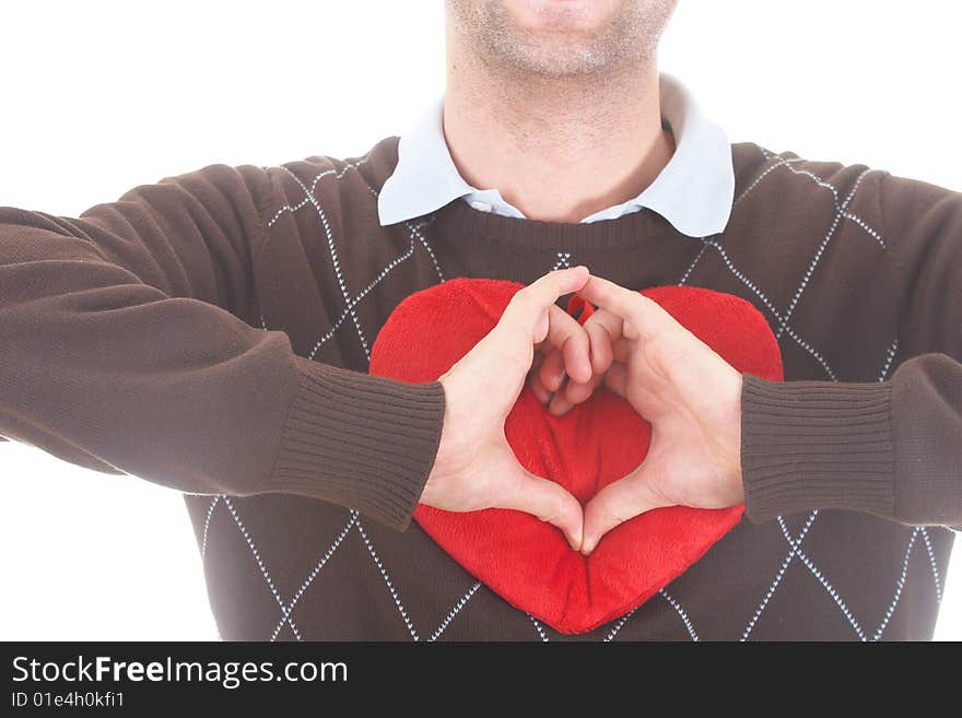 A young man shows a heart shape with his hands on a red heart-shaped pillow. Isolated over white.