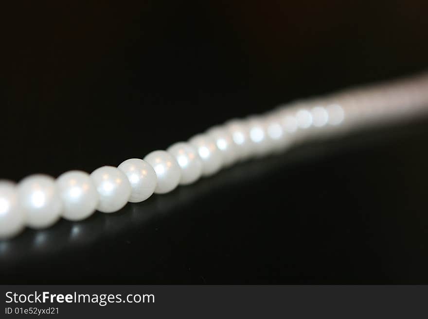 Pearl necklace lying on black table with reflection