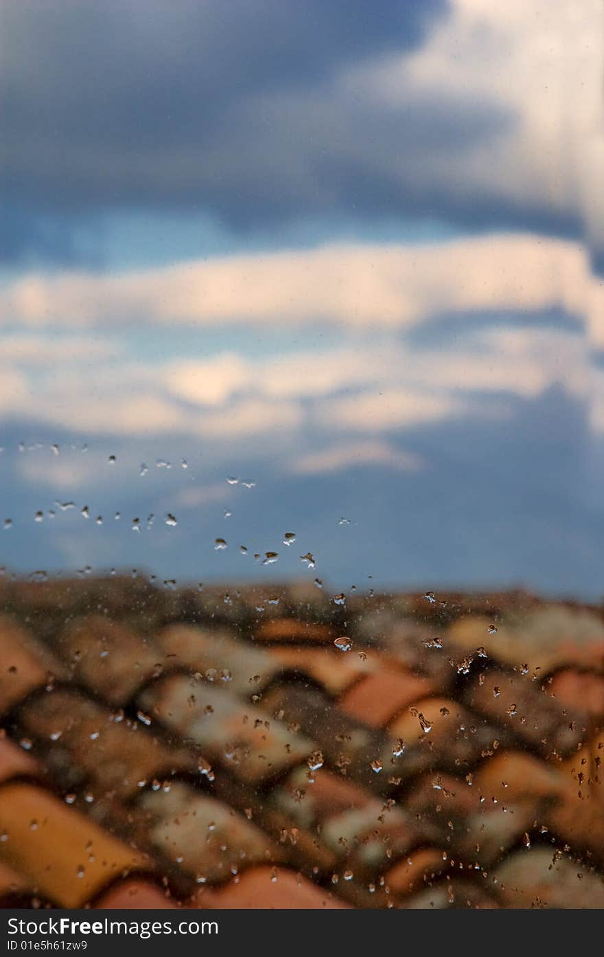 Water drops on window pane with roof and clouds in the distance. Shallow depth of field and copy space. Water drops on window pane with roof and clouds in the distance. Shallow depth of field and copy space.