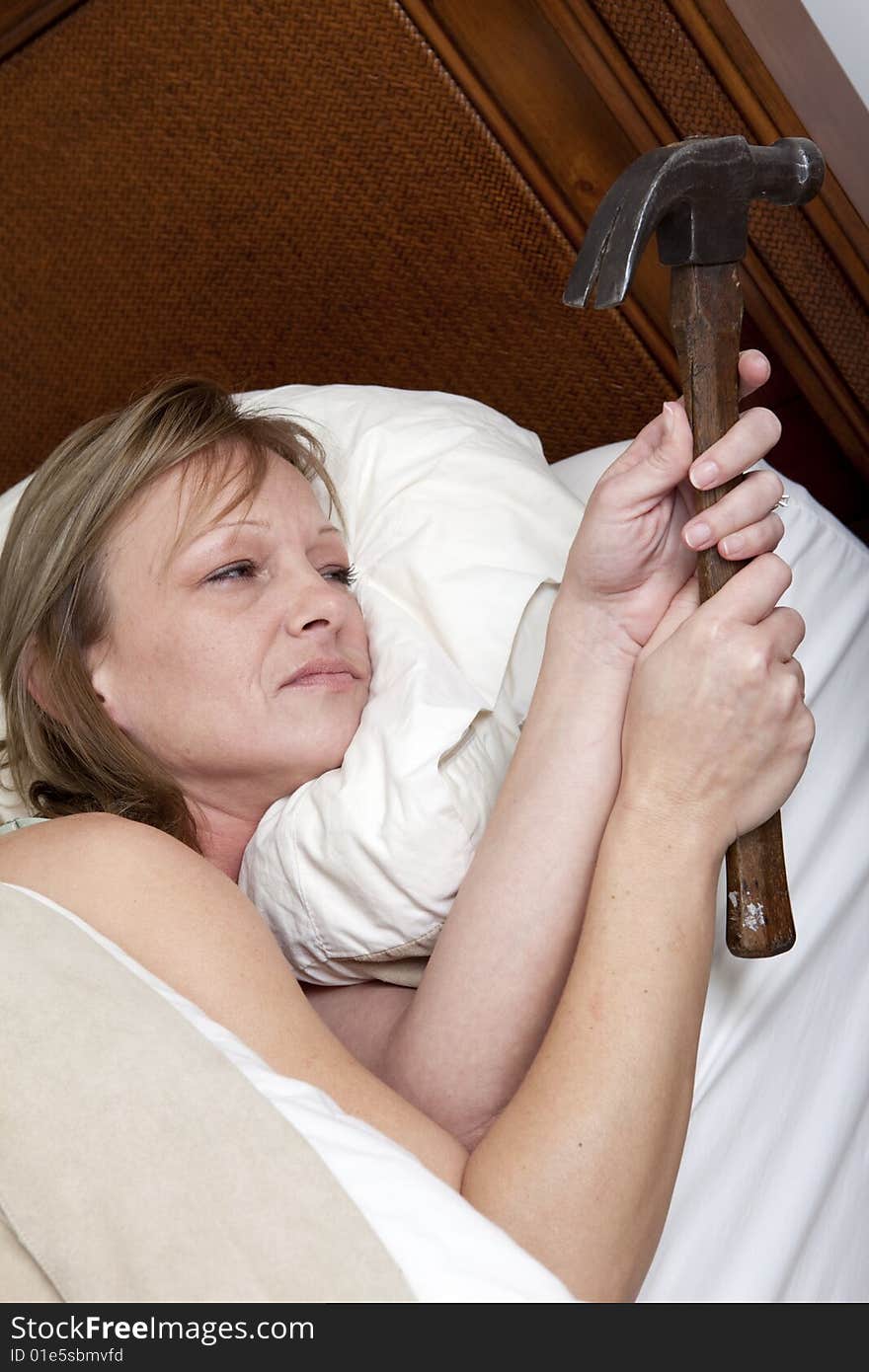 A tired woman in bed holding a hammer ready to strike. A tired woman in bed holding a hammer ready to strike