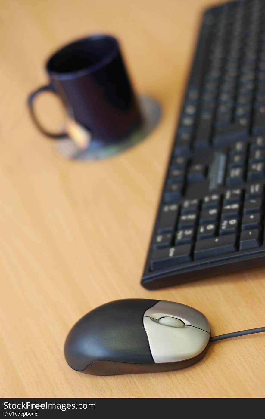 Computer mouse, keyboard and cup on the wooden table. Break for tea