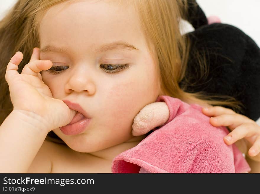 Beautiful baby girl sucking on her thumb and hugging her doll in cot just before bedtime