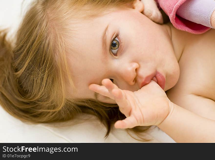 Beautiful baby girl sucking her thumb and hugging her doll in her cot just before bedtime