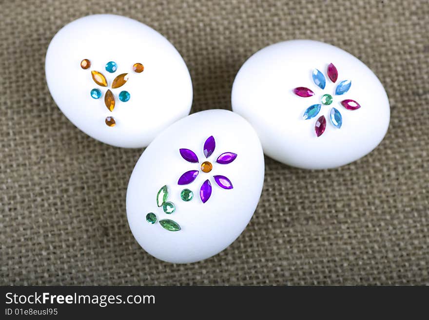 Three easter eggs with jewels on them sitting on a piece of burlap