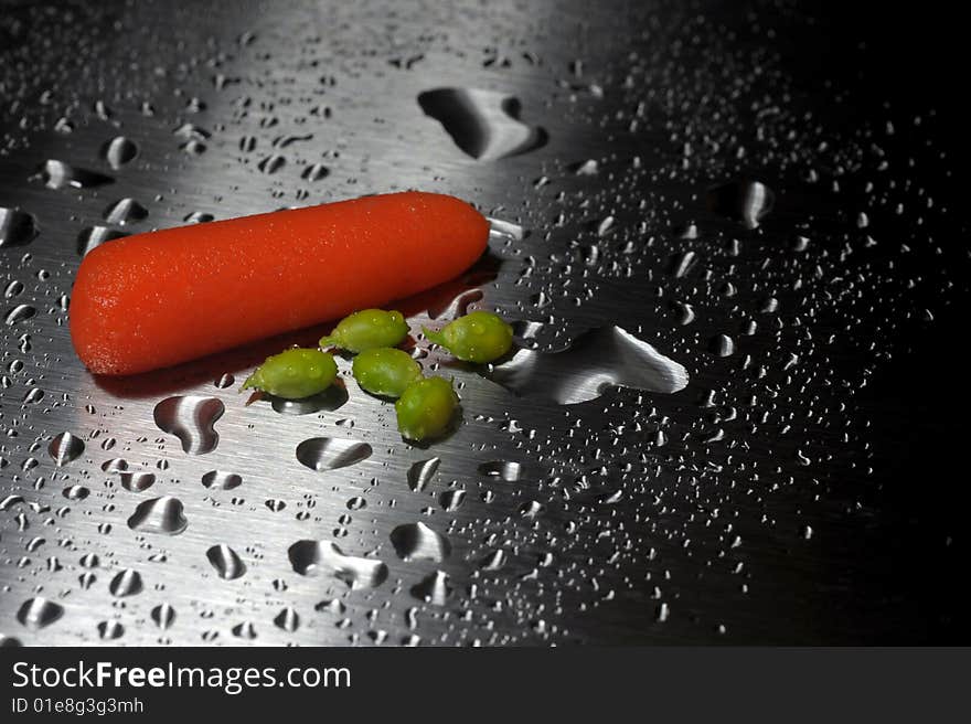 Single baby carrot and a few peas on a silver sheet with water drops. Single baby carrot and a few peas on a silver sheet with water drops