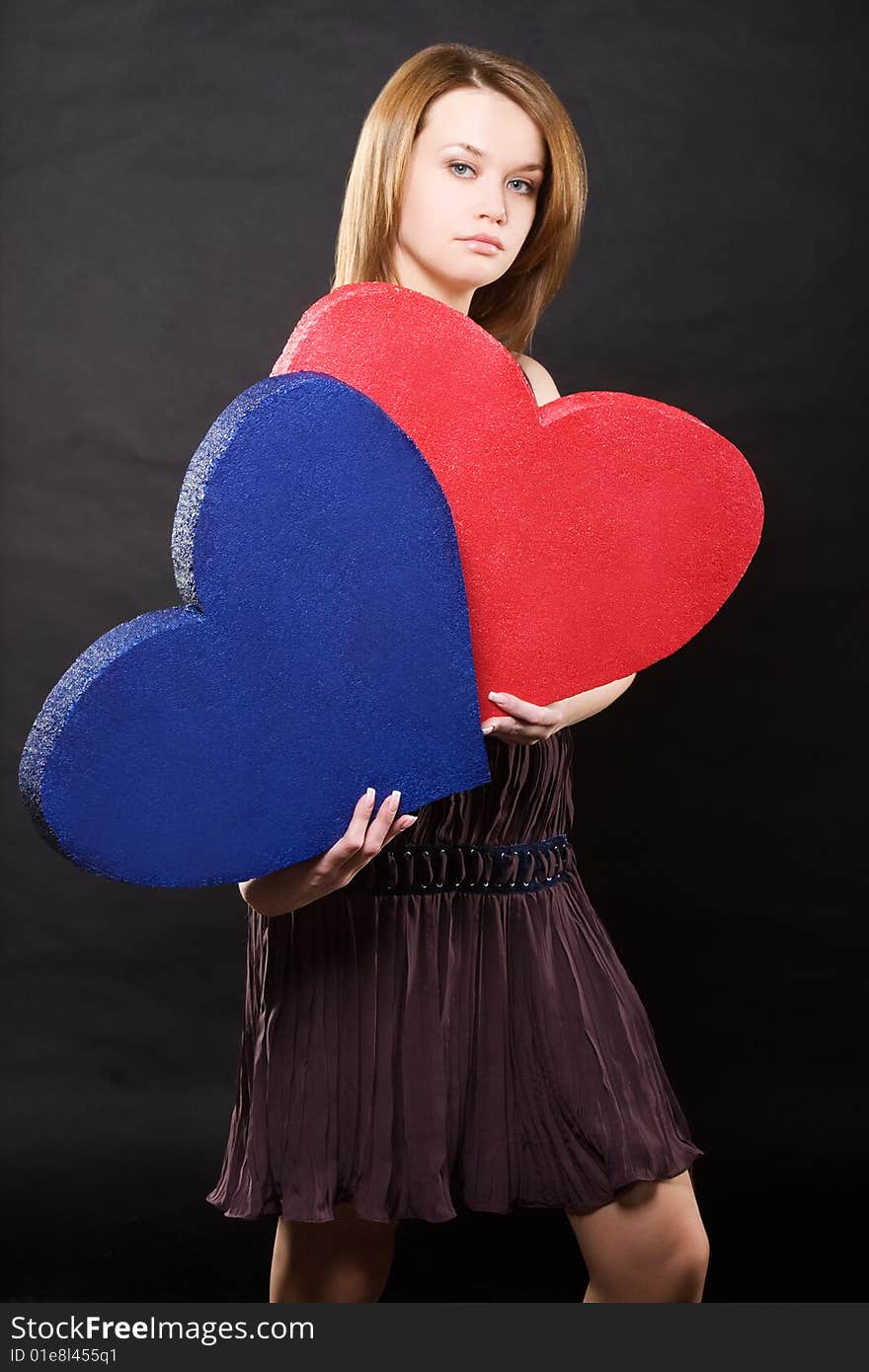 Pretty girl in dress holding two hearts over black background