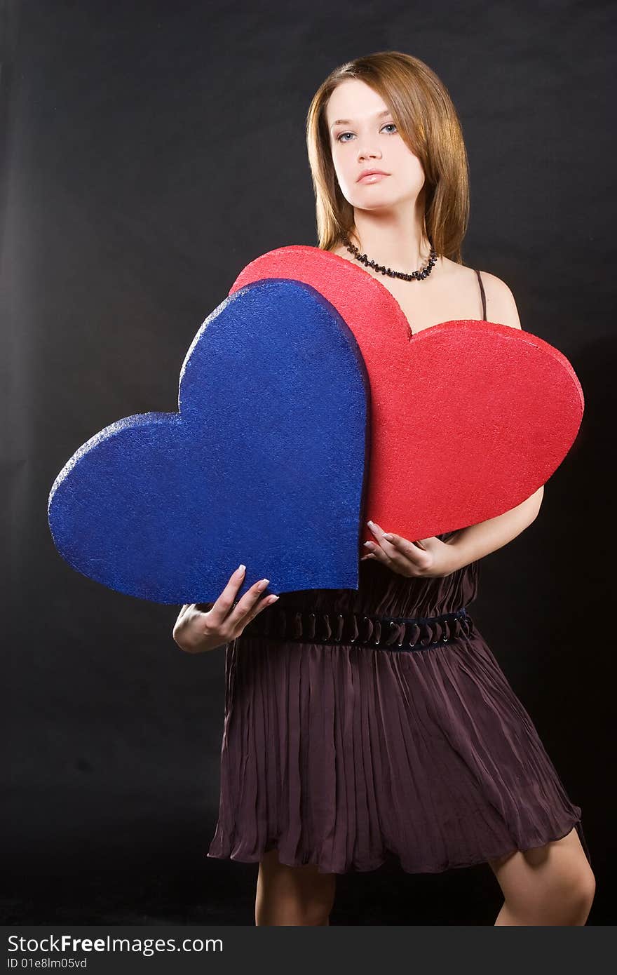 Girl in dress holding two hearts  over black background